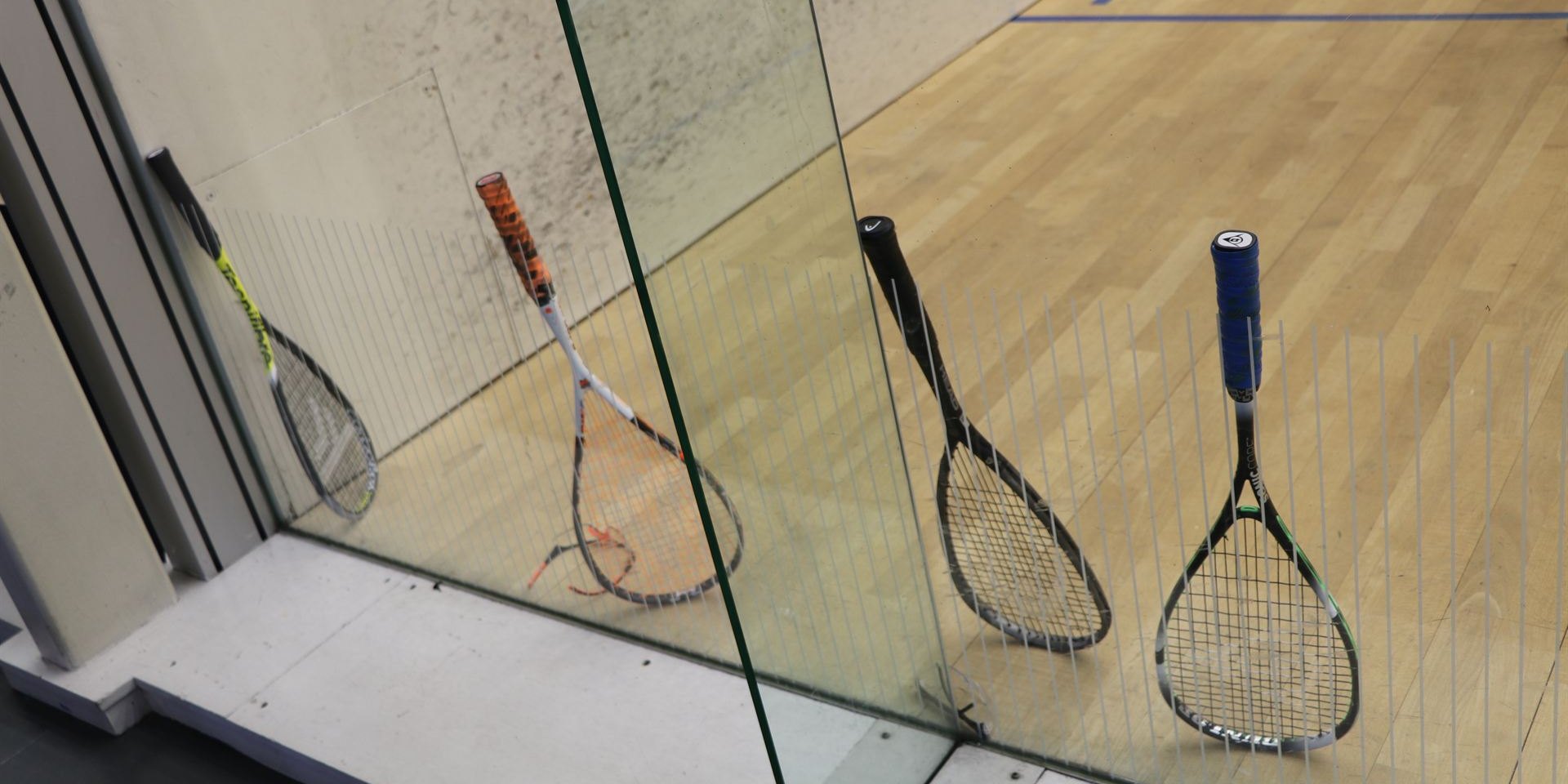 Squash rackets resting against the glass wall of a court