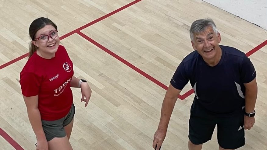 Two squash players laughing together on court, one younger and one older