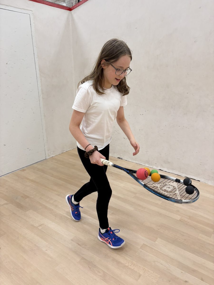 A young player balancing squash balls on her racket