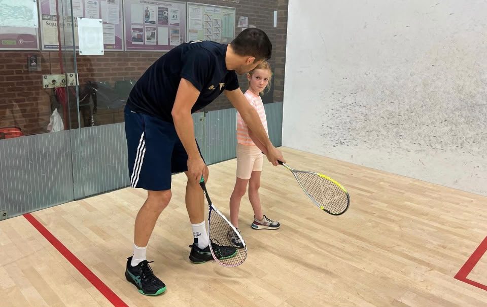 A coach showing a young girl how to hold a squash racket