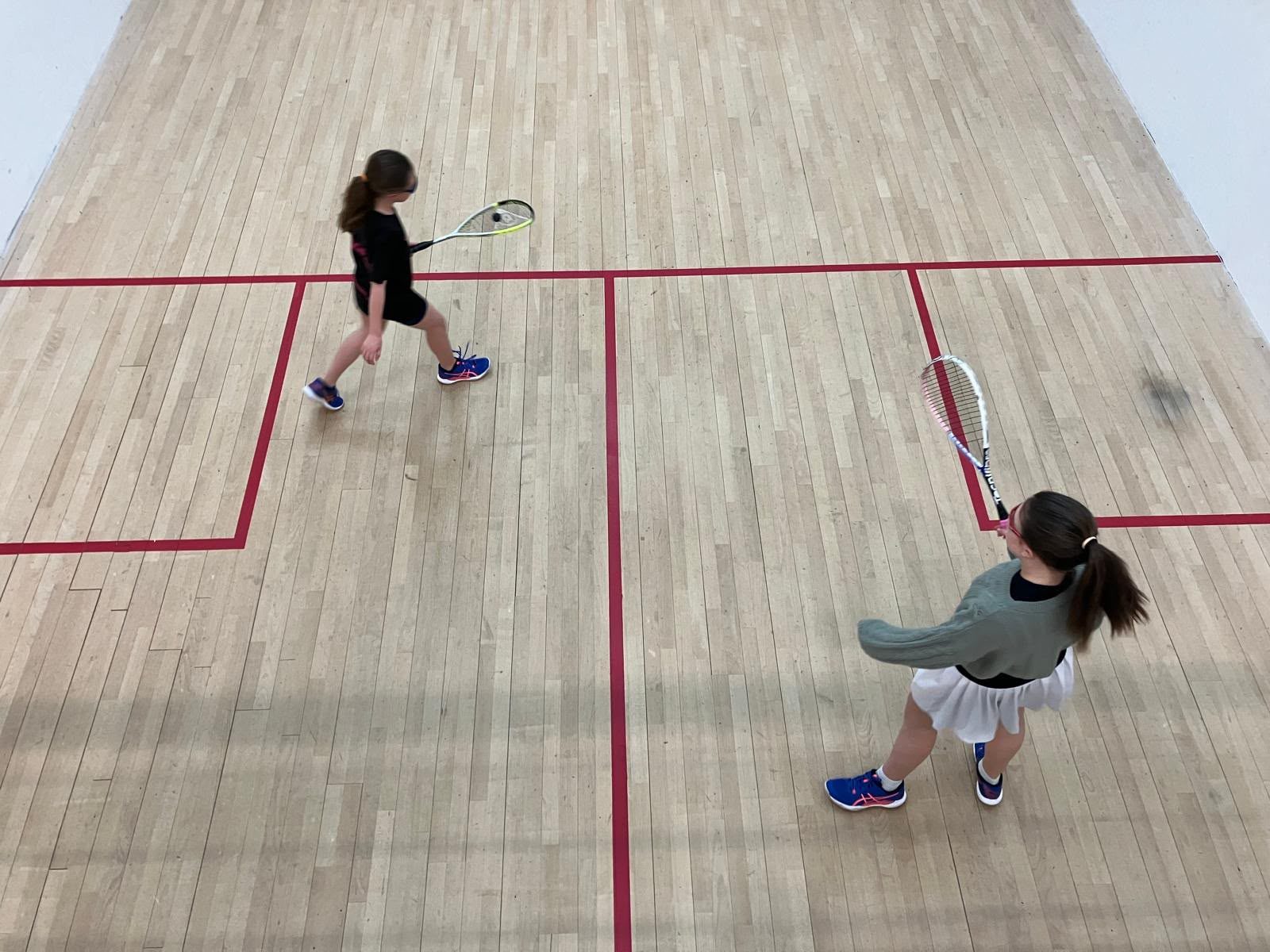 Two young players rallying on a squash court