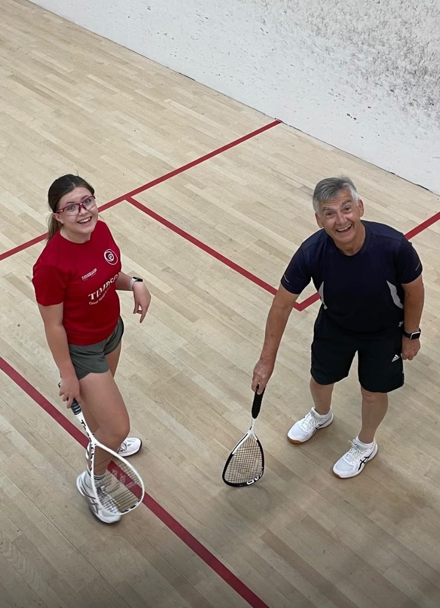 A teenager and her grandad smiling on a squash court